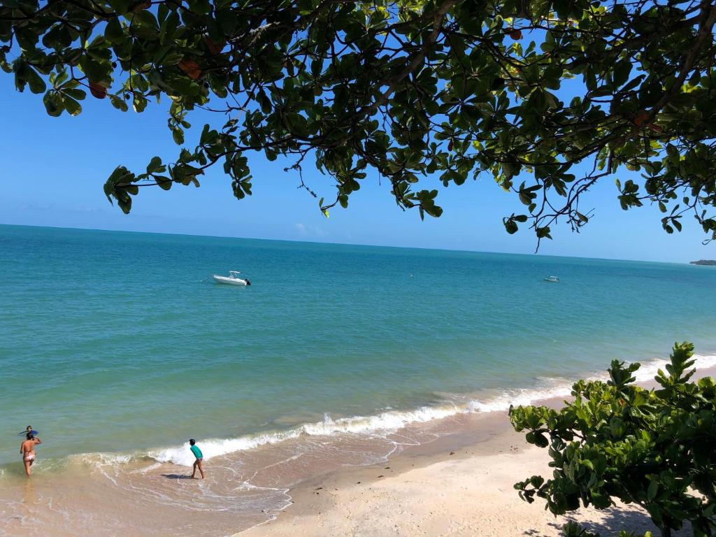 Praia da Vila de Corumbau com mar azul e turquesa, banhistas na beira da água e barcos ancorados ao longe na Bahia. Praia da Vila de Corumbau com mar azul e turquesa, banhistas na beira da água e barcos ancorados ao longe na Bahia.