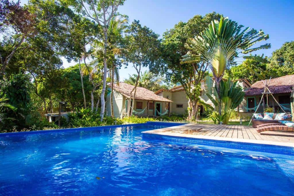 Área de lazer da Pousada Le Refuge em Trancoso, com deck de madeira, poltronas confortáveis e piscina cercada por vegetação nativa Área de lazer da Pousada Le Refuge em Trancoso, com deck de madeira, poltronas confortáveis e piscina cercada por vegetação nativa