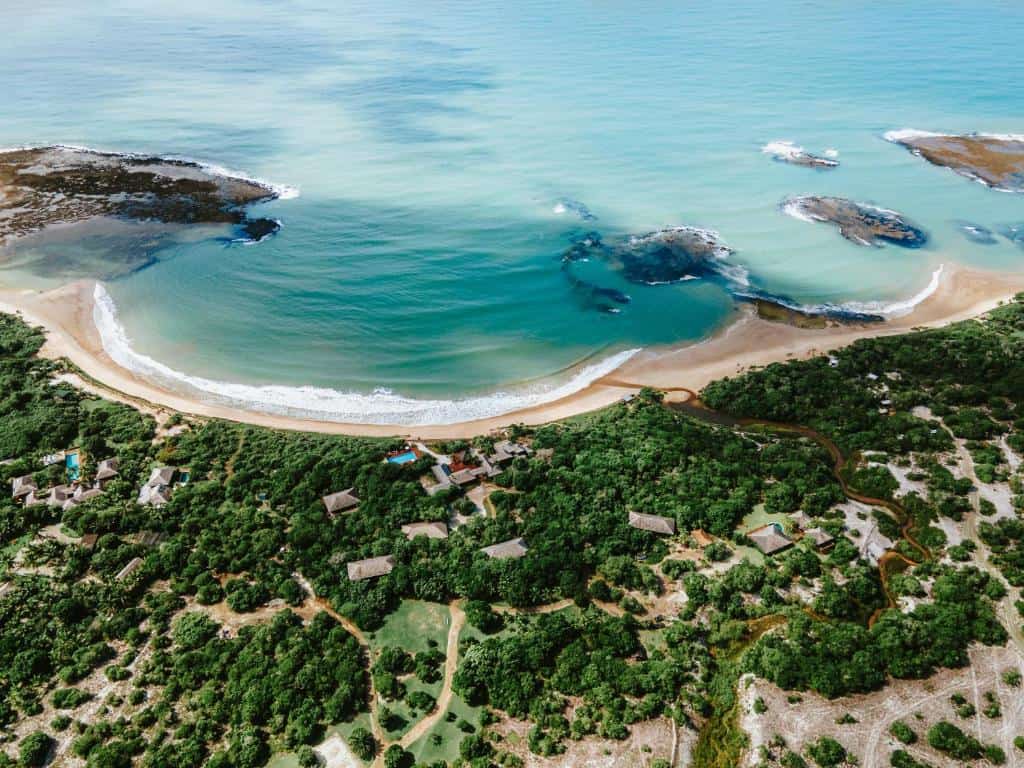 Vista aérea da Praia de Itapororoca em Trancoso, destacando o litoral recortado, as piscinas naturais e a estrutura da Pousada Tutabel entre a vegetação Vista aérea da Praia de Itapororoca em Trancoso, destacando o litoral recortado, as piscinas naturais e a estrutura da Pousada Tutabel entre a vegetação