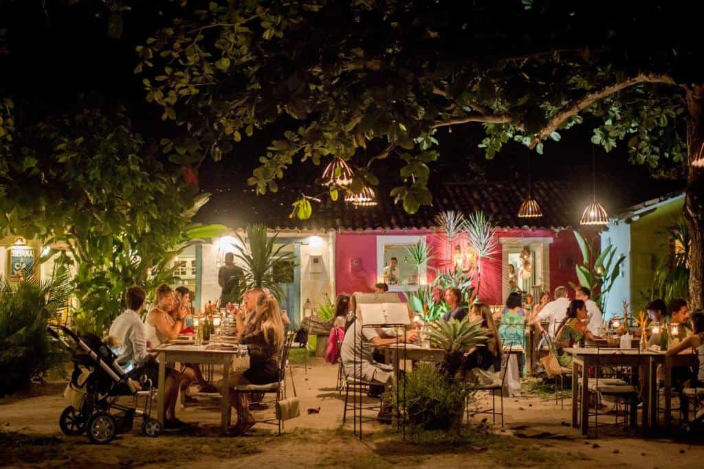 Fachada de casinha colorida transformada em restaurante no Quadrado de Trancoso, com mesas ao ar livre iluminadas por luminárias rústicas à noite Fachada de casinha colorida transformada em restaurante no Quadrado de Trancoso, com mesas ao ar livre iluminadas por luminárias rústicas à noite.